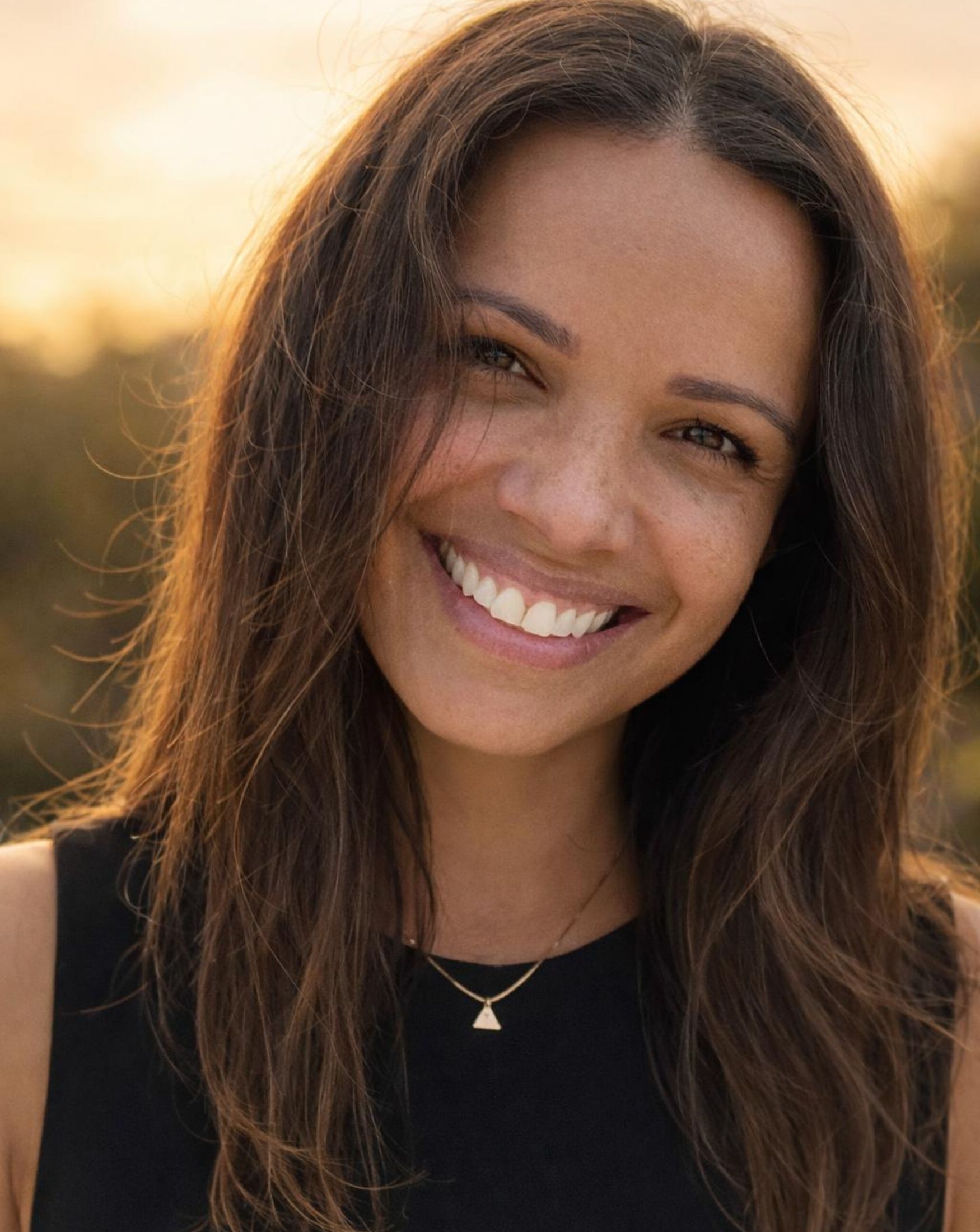 Sara Liyanage-Denney, founder of KINSPACE — portrait headshot, golden hour light, wearing a black top with a small triangle pendant necklace