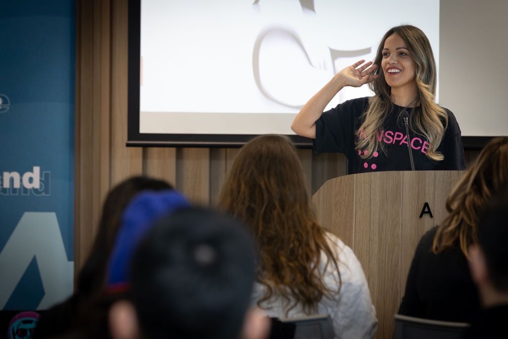 Sara Liyanage-Denney speaking at a WiET event, mid-gesture at a podium with an engaged audience